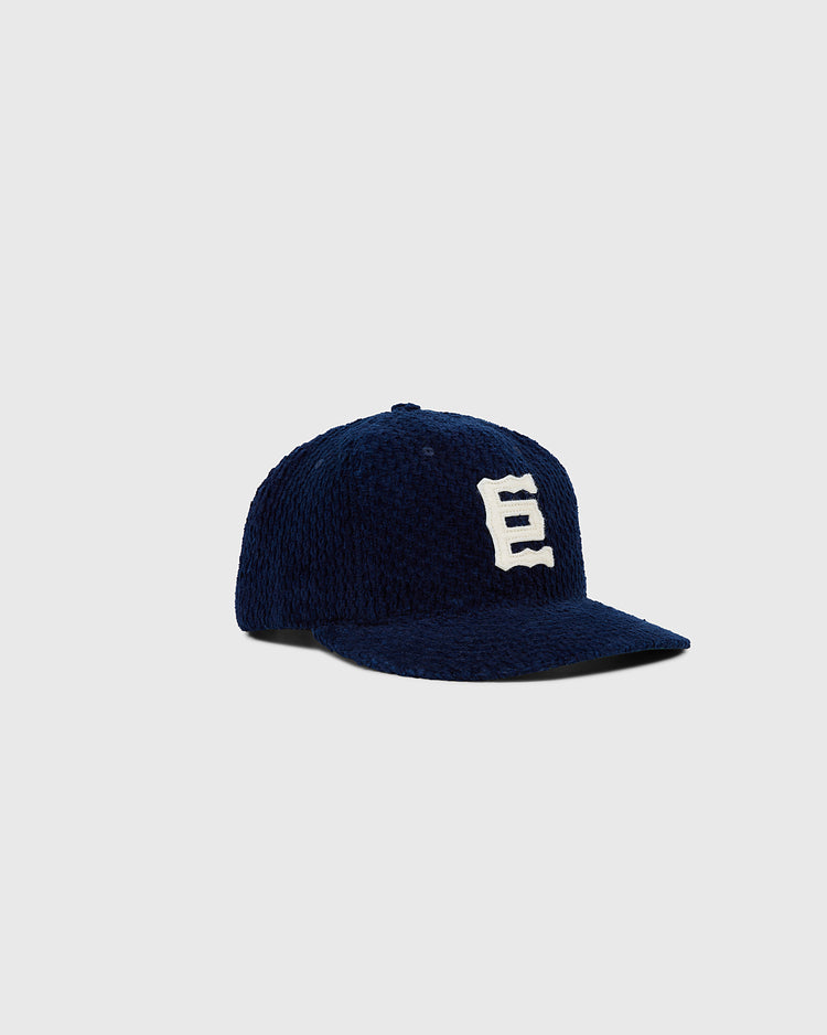 The Tokyo Giants Japanese Indigo Corduroy Ballcap by Ebbets Field features a bold white “E” on navy blue indigo-dyed corduroy, shown against a light gray background—ideal for Japanese baseball memorabilia fans.
