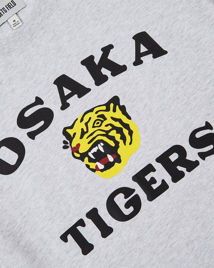 The Ebbets Field Osaka Tigers Short Sleeve Graphic Tee features bold black text and a yellow roaring tiger face on gray, inspired by classic Japanese baseball shirts and Koshien Field style.