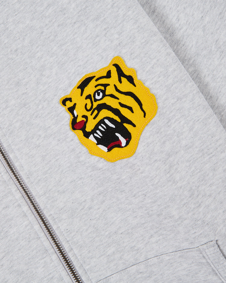 A close-up of the Ebbets Field Osaka Tigers Heavyweight Cotton Terry Full-Zip Hoodie, featuring a vintage-style patch of a roaring yellow tiger's head with an open mouth, red tongue, and black stripes sewn near the zipper.