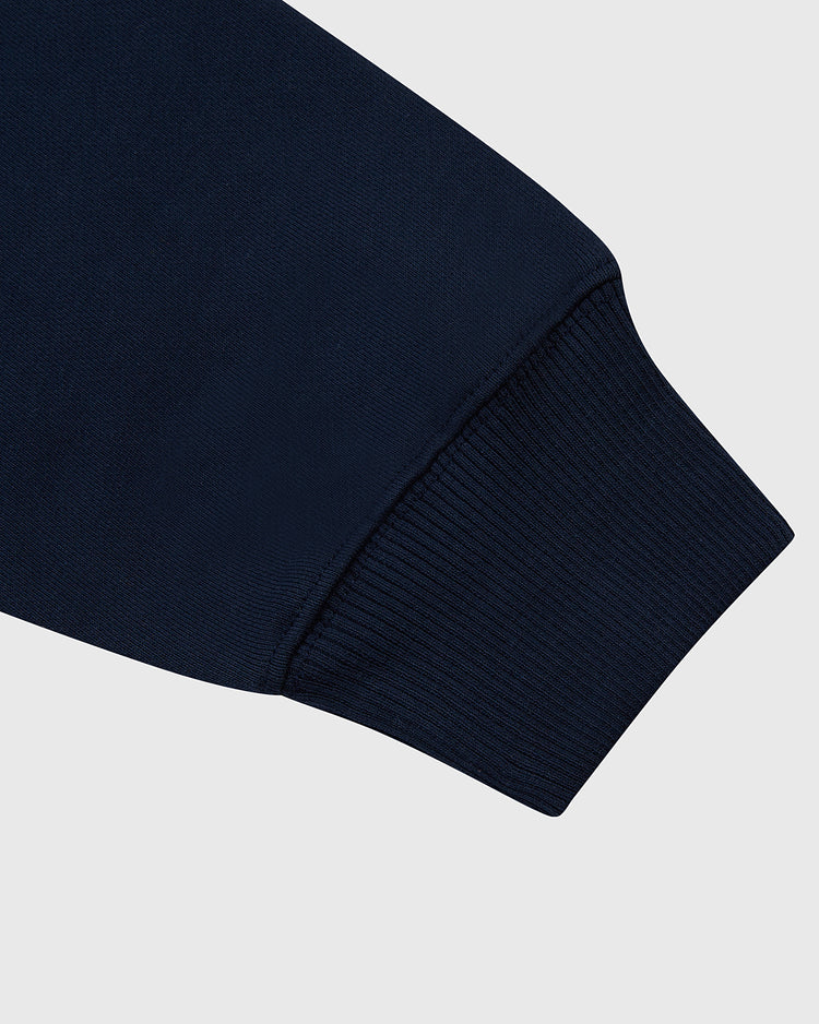 Close-up of the Ebbets Field Brooklyn Eagles Heavyweight Cotton Terry Pullover Hoodie sleeve shows the ribbed cuff and subtle NY logo in navy blue, set against a plain light gray background.