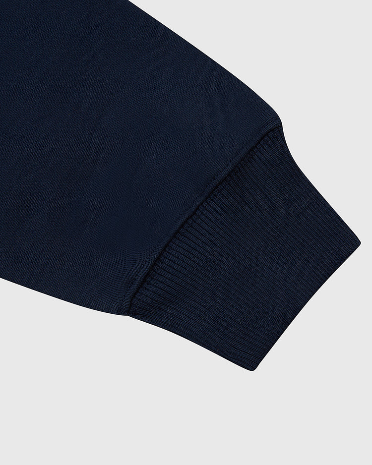 Close-up of a navy blue Ebbets Field USA 1960 Miracle On Ice Heavyweight Cotton Terry Pullover Hoodie sleeve with a ribbed cuff, set against a plain light gray background.