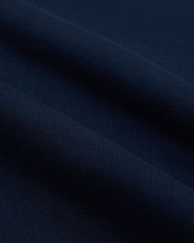 Close-up of dark navy blue cotton terry fabric with fine ribbed texture and soft folds, seen on the Ebbets Field Brooklyn Eagles Heavyweight Pullover Hoodie, creating gentle diagonal lines and subtle shadows.
