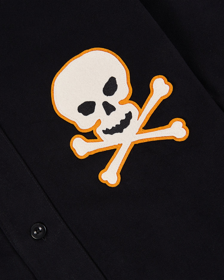 A white skull and crossbones patch with an orange outline is sewn near a black button on the Ebbets Field Sioux City Ghosts Cotton Twill Baseball Jersey, echoing the rebellious spirit of vintage sportswear.