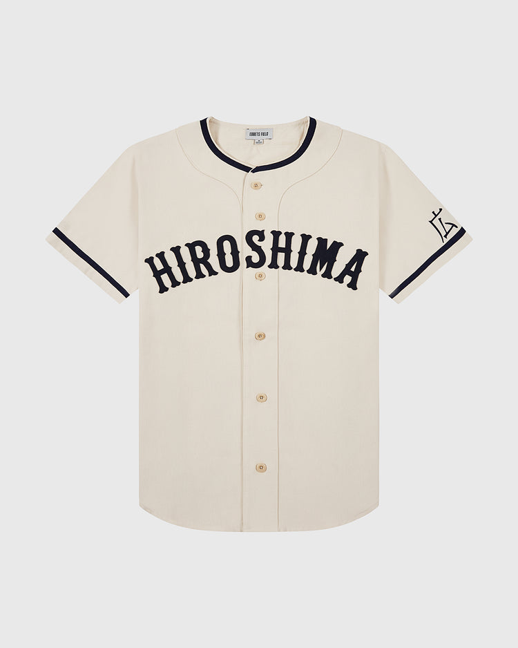 The Ebbets Field Hiroshima Carp Cotton Twill Baseball Jersey features cream cotton twill, “HIROSHIMA” in bold black on the chest, black sleeve trim, a left-sleeve graphic, and a classic button-down front.