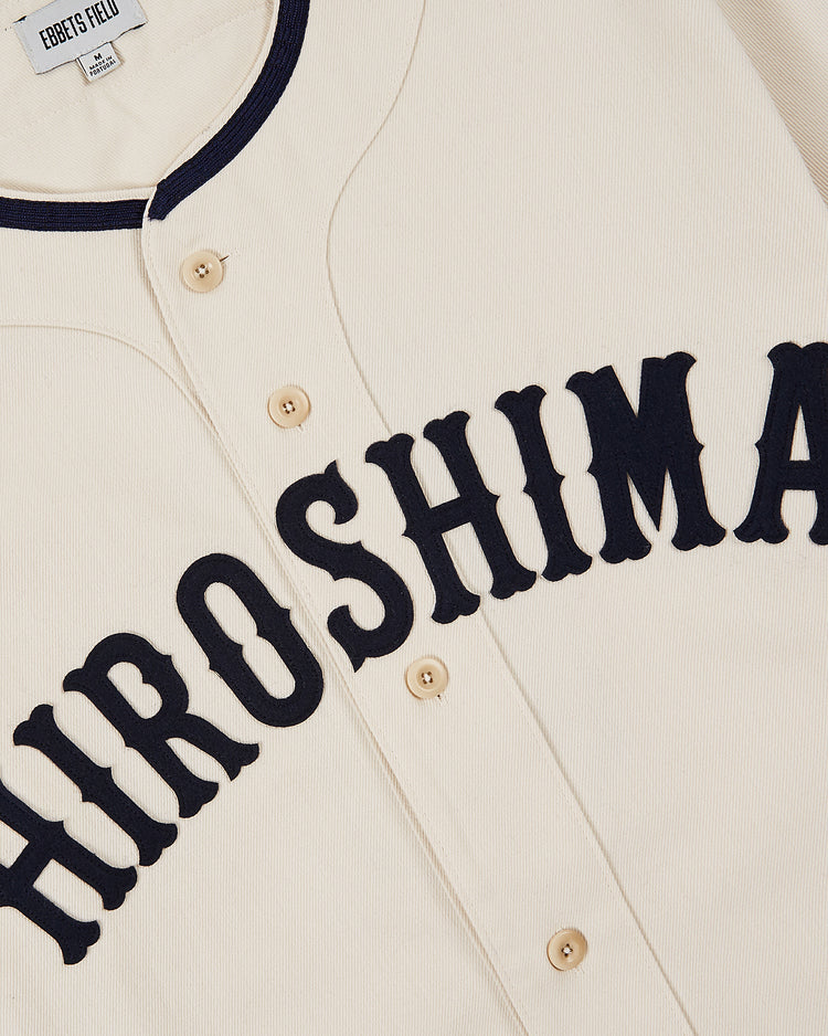 The Ebbets Field Hiroshima Carp Cotton Twill Baseball Jersey features a cream color with black trim and buttons, bold black 