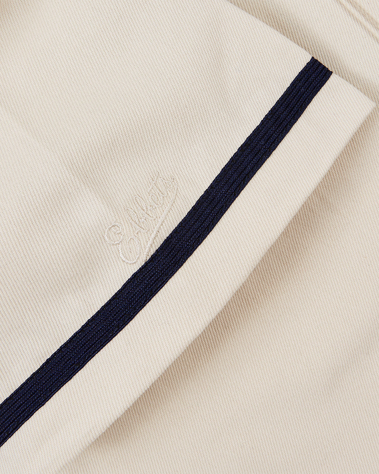 Close-up of Ebbets Field’s Hiroshima Carp Cotton Twill Baseball Jersey: light beige ribbed fabric with a dark navy diagonal stripe and subtle embroidered branding, capturing the classic texture and style of a vintage baseball jersey.