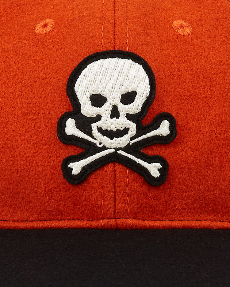 A close-up of the EFF Sioux City Ghosts 1935 Authentic Wool Softbrim Ballcap in orange, showcasing a white skull and crossbones outlined in black on the front and a contrasting black brim.