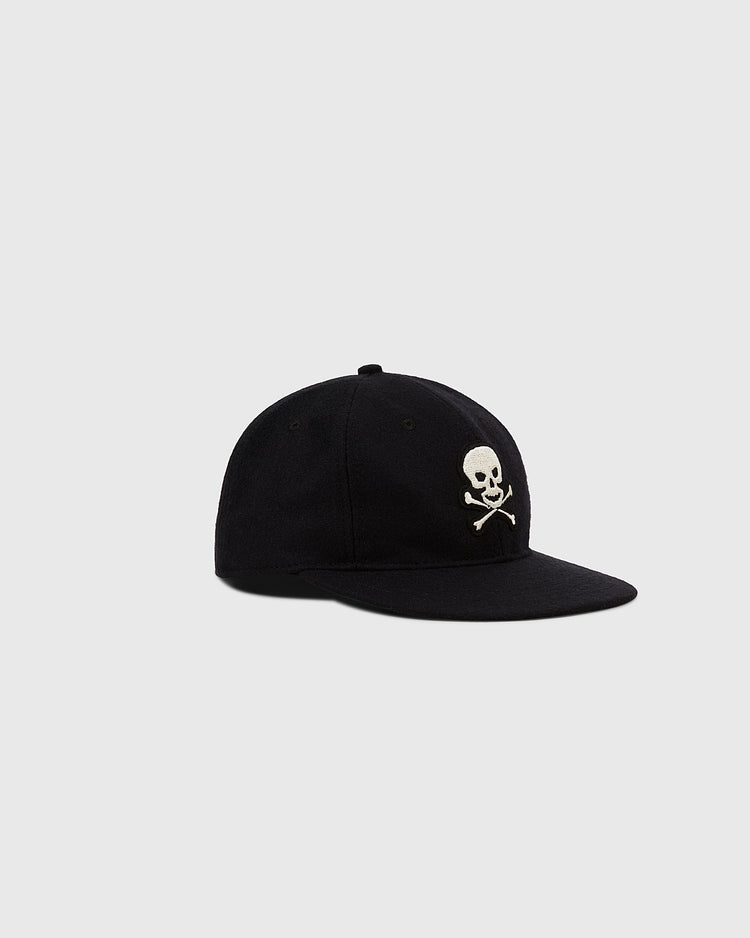 The Ebbets Field Sioux City Ghosts Vintage Inspired Wool Ballcap is a black cap with a white skull and crossbones on the front, evoking fast-pitch softball spirit, shown here on a plain light gray background.
