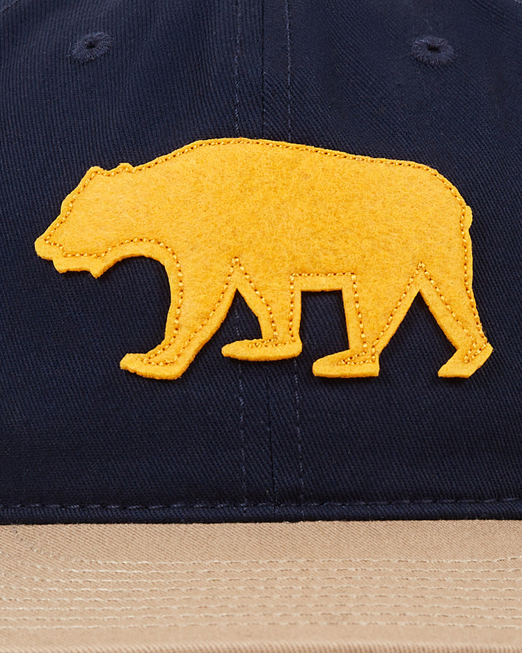 The Ebbets Field Mission Bears Cotton Twill Ballcap features a navy crown, tan brim, and yellow felt bear silhouette—an homage to Bay Area baseball history and inspired by the 1926 Mission Bears hat.