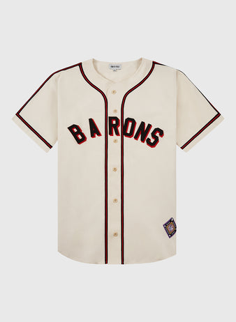 The Ebbets Field Birmingham Black Barons Cotton Twill Jersey features a cream color with black and red trim, black BARONS lettering across the chest, and a patch near the hem, honoring legends like Satchel Paige and Willie Mays.