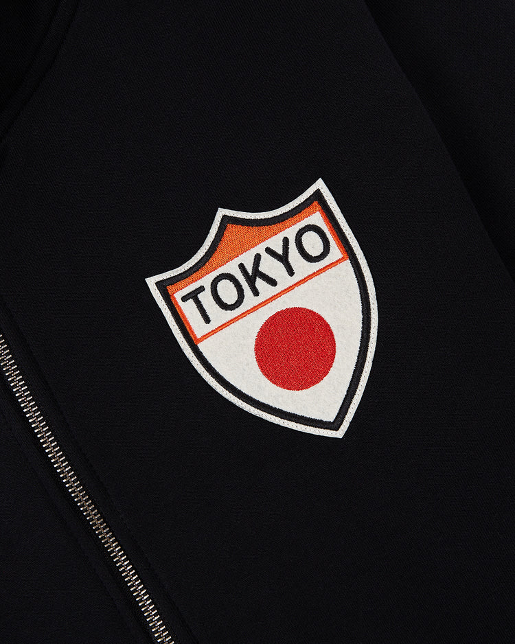 The Ebbets Field Tokyo Giants Heavyweight Cotton Terry Full-Zip Hoodie features a black vintage design with a shield-shaped “TOKYO” patch and red circle, inspired by the Japanese flag, next to the zipper.