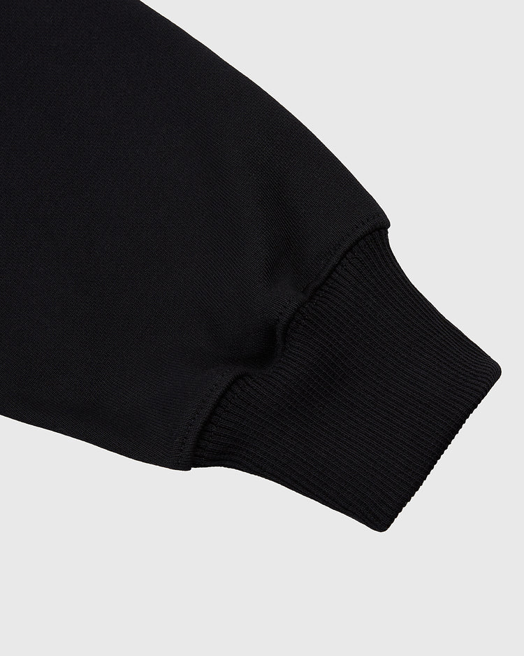 Close-up of the Ebbets Field Sioux City Ghosts Double Felt Heavyweight Cotton Terry Pullover Hoodie in black, highlighting the ribbed, fitted cuff and sleeve against a light gray background.