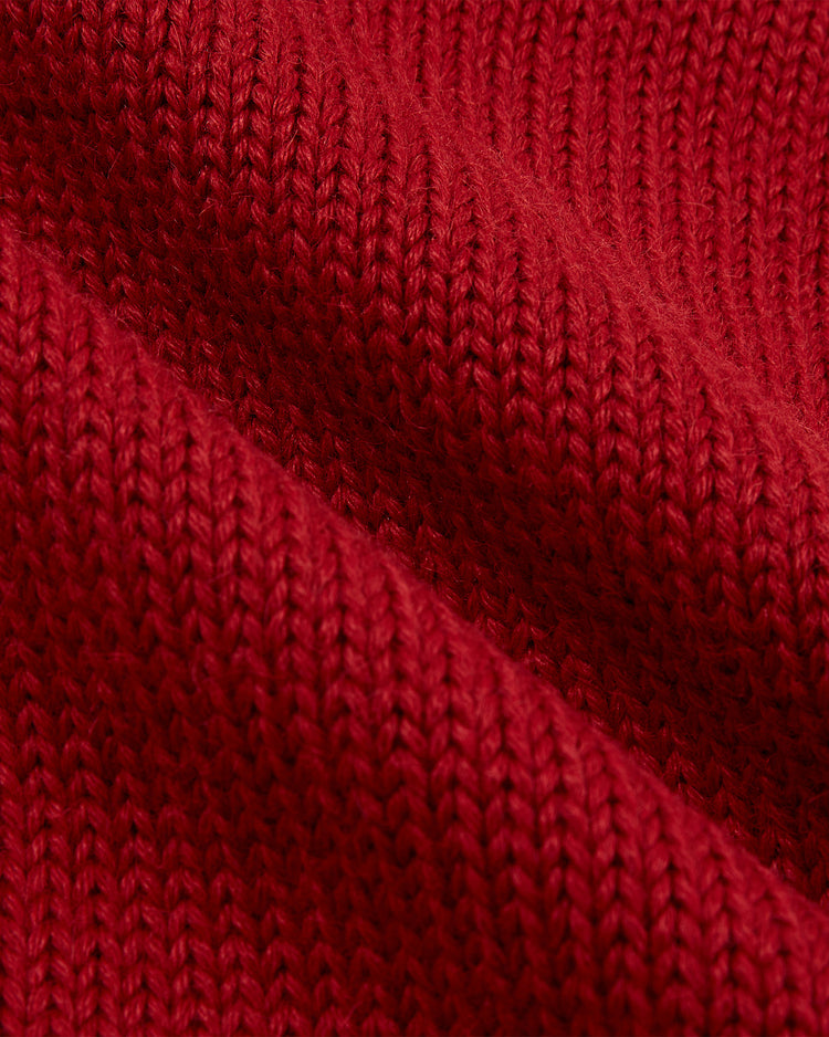 Close-up of EFF’s Boston Red Sox 1924-1960 Wool Shawl Collar Sweater shows textured red knit with diagonal ribs and tightly woven yarns, shadows highlighting the pattern’s depth and structure.