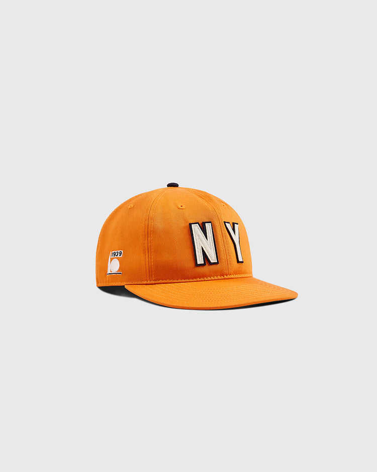 The Ebbets Field New York 1939 World's Fair Cotton Twill Ballcap is orange, featuring large white NY letters on the front and a small white 1939 patch on the left side, shown against a light gray background.