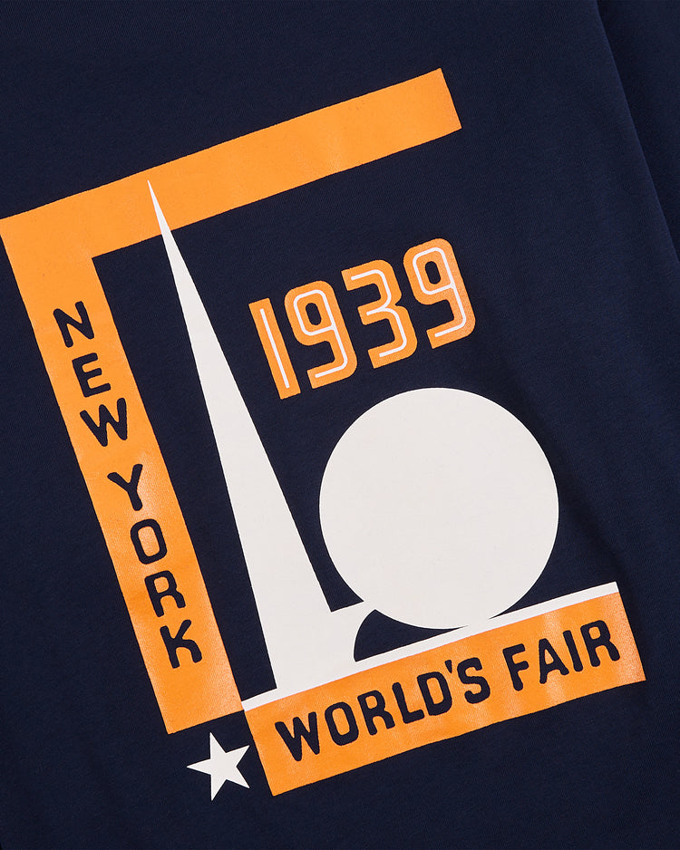 Ebbets Field's New York 1939 World's Fair Long Sleeve Graphic Tee in navy features orange and white text, geometric shapes, a spike, globe, and star—offering a stylish tribute to the iconic World's Fair.