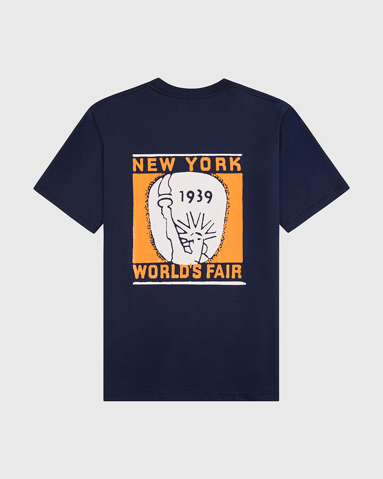 The Ebbets Field New York 1939 World's Fair Short Sleeve Graphic Tee is a navy blue shirt with a bold orange and white back graphic featuring “1939 World’s Fair,” “NEW YORK WORLD’S FAIR,” and an abstract Statue of Liberty design.