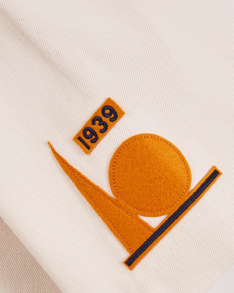 A close-up of white cotton twill fabric from the Ebbets Field 1939 WORLD'S FAIR JERSEY features orange and black embroidery with 