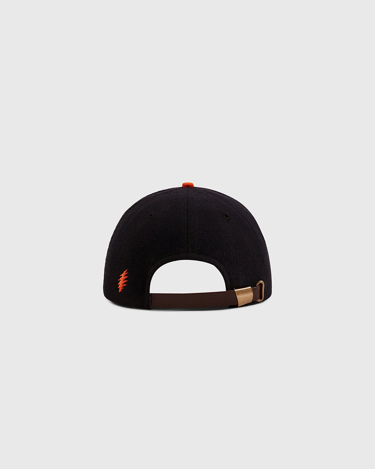 The Ebbets Field Grateful Dead Dancing Bear Wool Ballcap in black is shown from the back with an adjustable brown strap, metal clasp, and a small red dancing bear logo on the left side. The background is light gray.