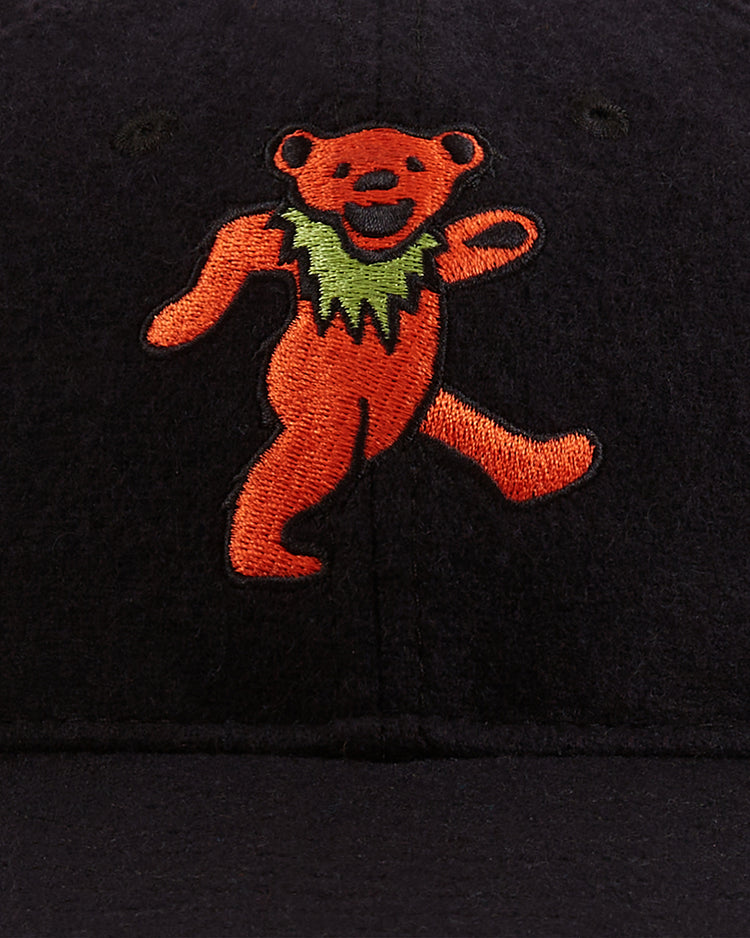 A close-up of the Grateful Dead Dancing Bear Wool Ballcap by Ebbets Field, featuring an embroidered orange dancing bear with a green collar, one arm raised, and one leg lifted.