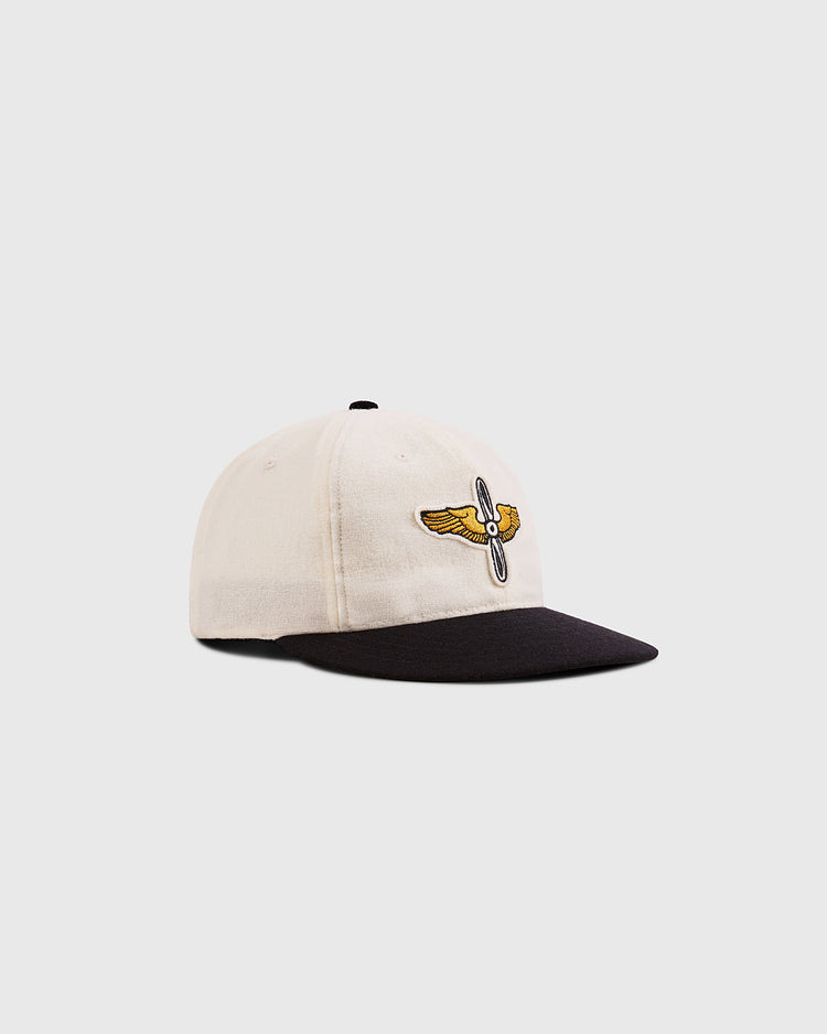 The Ebbets Field Mystery Caps of Mexico – Aviacion 1917 Authentic Wool Ballcap is beige with a black brim and an embroidered yellow and white winged propeller logo, celebrating Mexican baseball history. Shown on a plain light gray background.