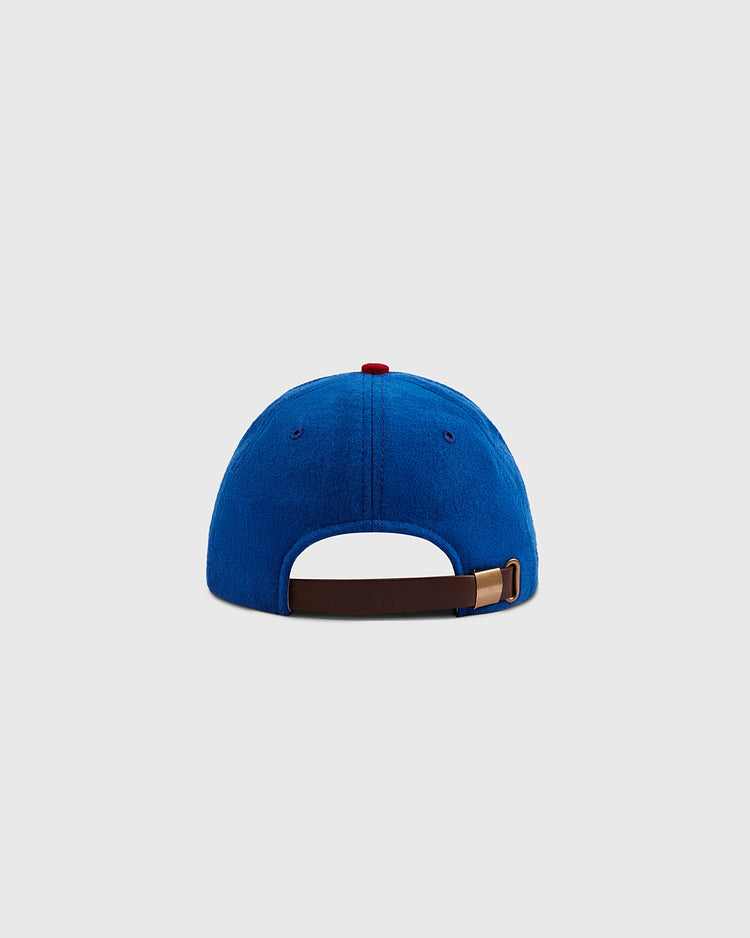 A blue Ebbets Field Sankei Atoms 1966 Vintage Inspired Wool Ballcap seen from the back, showcasing a brown adjustable strap with a gold buckle and a small red top button, set against a plain light gray background.