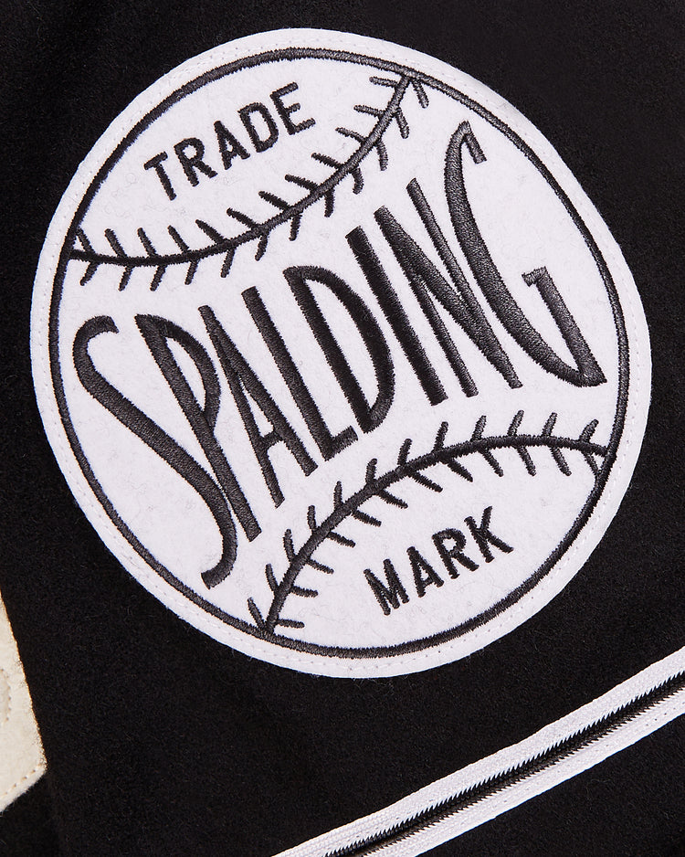 Close-up of a black and white patch on the Ebbets Field Babe Ruth Bustin' Babes Authentic Wool Baseball Jersey, featuring the Spalding logo, 