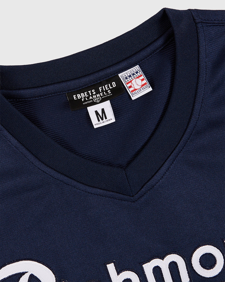 Close-up of the collar and tags on a navy blue Ebbets Field Tom Glavine Richmond Braves V-Neck Jersey, size medium, featuring partial white embroidered lettering in a style reminiscent of classic Atlanta Braves jerseys.
