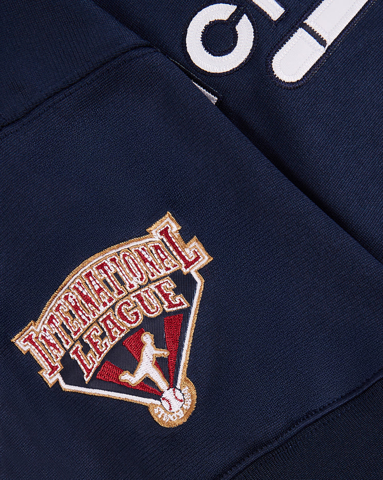 Close-up of an Ebbets Field Tom Glavine Richmond Braves V-Neck Jersey in dark blue, displaying a white number and an embroidered INTERNATIONAL LEAGUE patch above a baseball player silhouette over home plate.