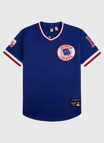 The Greg Maddux Peoria Chiefs V-Neck Jersey by Ebbets Field is a blue minor league jersey with red and white trim, a large Peoria Chiefs patch on the left chest, team logos on the sleeves, and an Ebbets Field label above the front hem.