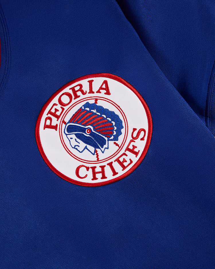A circular patch on blue fabric shows PEORIA CHIEFS in red around a feathered headdress profile, just like the one on the Greg Maddux Peoria Chiefs V-Neck Jersey by Ebbets Field.