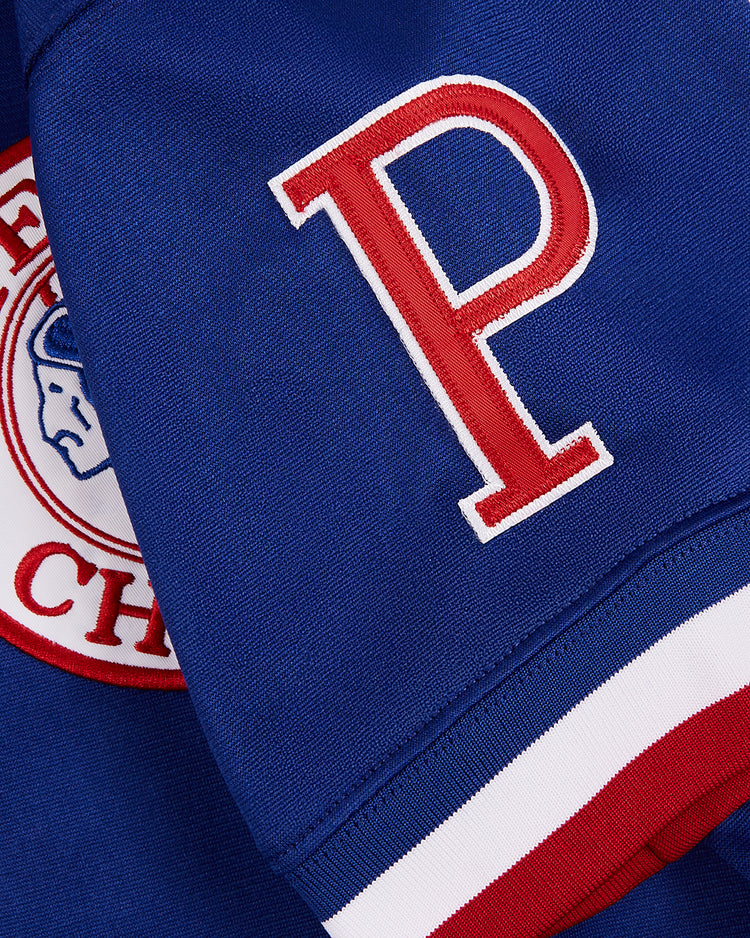 A close-up of the Ebbets Field Greg Maddux Peoria Chiefs V-Neck Jersey shows its blue fabric, prominent red and white 
