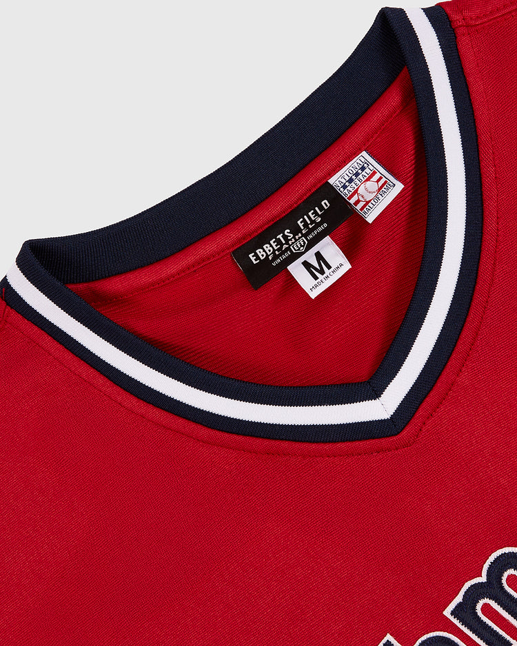 A close-up of the Ebbets Field John Smoltz Richmond Braves V-Neck Jersey in red shows a navy and white striped collar, Ebbets Field label, medium size tag, and part of the front lettering recalling his minor league days.