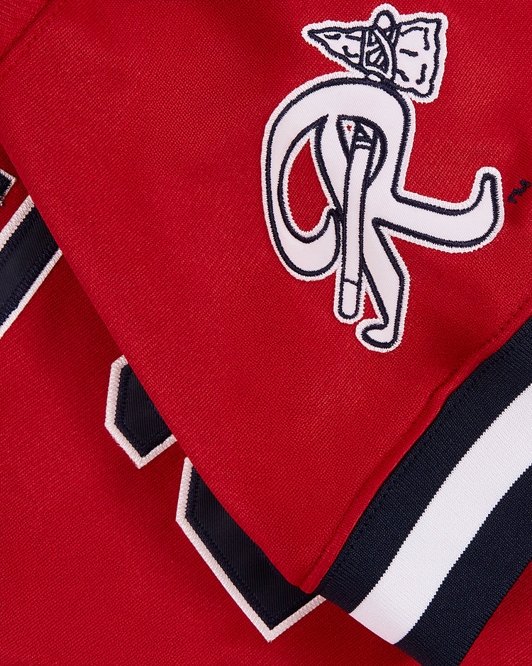 Close-up of the Ebbets Field John Smoltz Richmond Braves V-Neck Jersey in red, featuring a white embroidered R with a pizza slice detail and white and navy striped edging.