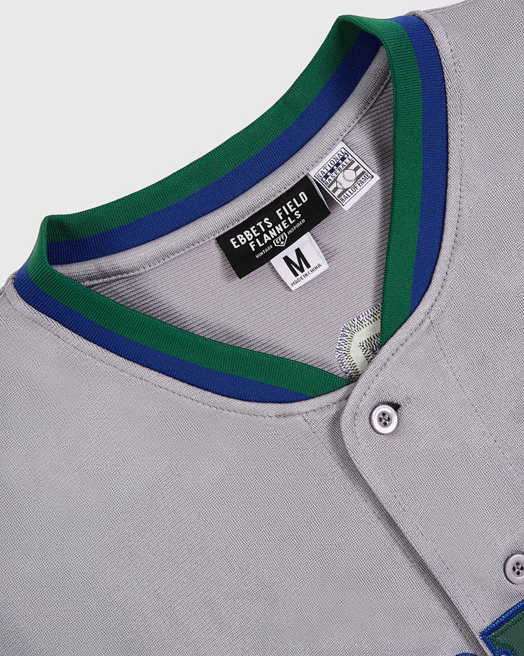 Close-up of a gray Barry Larkin Denver Zephyrs Button Up Jersey with green and blue collar trim. Inner tags display the Ebbets Field brand and size M (medium).