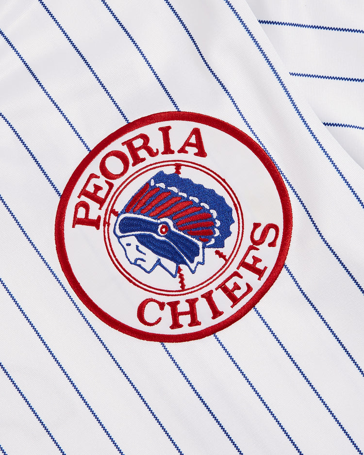 Close-up of the Greg Maddux Peoria Chiefs V-Neck Jersey by Ebbets Field, white with blue pinstripes and a circular Peoria Chiefs logo featuring a Native American chief in a feathered headdress—a classic minor league look.