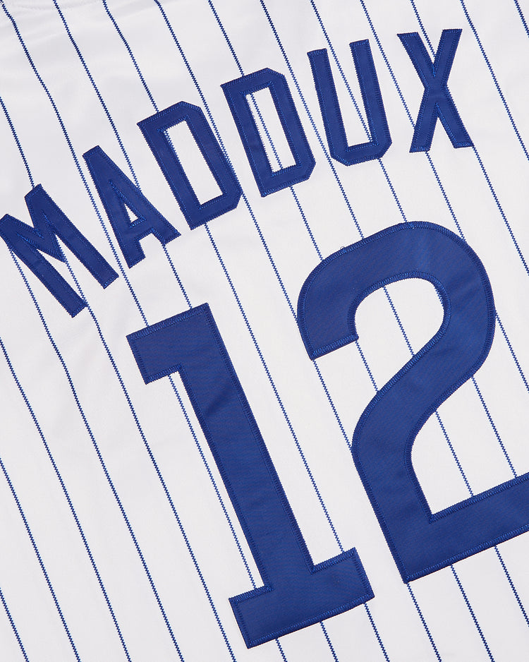 The Ebbets Field Greg Maddux Peoria Chiefs V-Neck Jersey is white with blue pinstripes, featuring “MADDUX” and number 12 in bold blue, inspired by his minor league days.