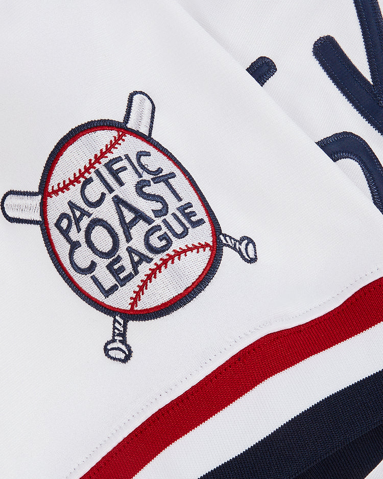 A close-up of the Ebbets Field Jim Thome Colorado Springs Sky Fox Button Up Jersey shows a white patch with a baseball, crossed bats, red and navy stripes, and “Pacific Coast League” embroidery—evoking classic minor league jersey style.
