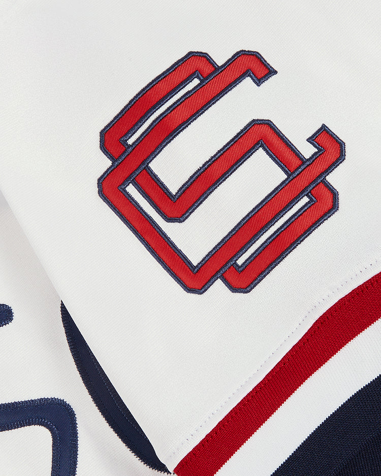 Close-up of the Ebbets Field Jim Thome Colorado Springs Sky Fox Button Up Jersey, featuring white fabric, an interlocking red and navy double C logo, and a red, white, and navy striped trim along the edge.