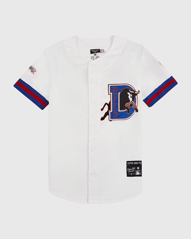 The Chipper Jones Durham Bulls Button Up Jersey by Ebbets Field is a white jersey with blue and red-striped sleeves, a large bull logo on the left chest, and several patches—ideal for Atlanta Braves memorabilia collectors.