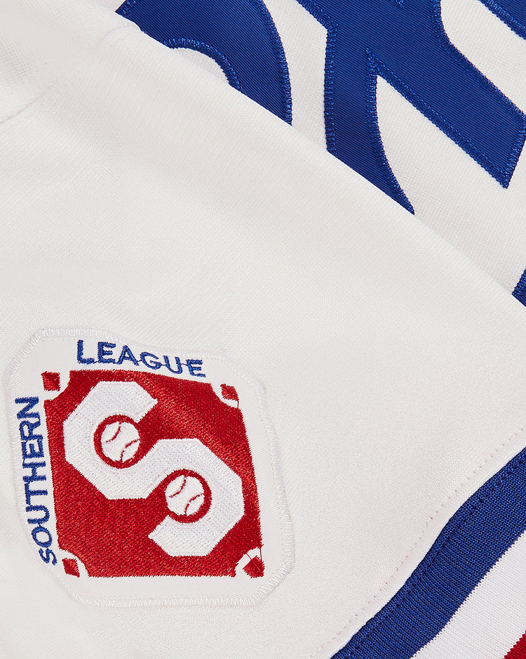 Close-up of a white Ebbets Field Tim Raines Memphis Chicks Button Up Jersey, showing the red and white Southern League patch with two baseballs and a large S, plus part of a blue embroidered number in the background.