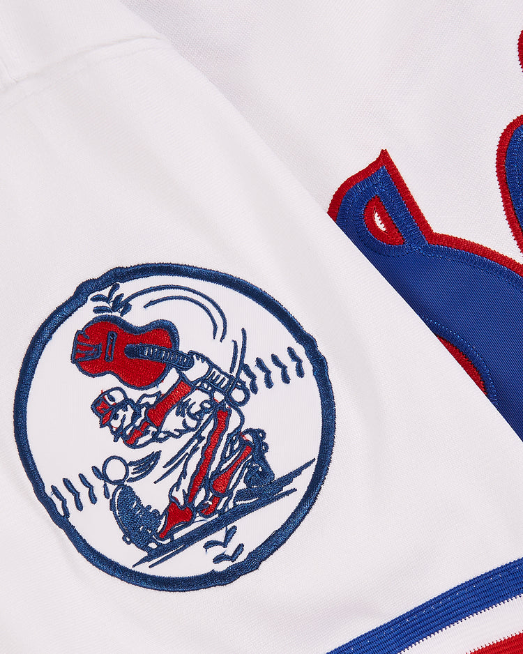Close-up of the Nashville Sounds EFF MiLB Button Down Jersey by EFF, showing a circular patch with a red and blue cartoon baseball player swinging a bat, stitch marks around the edge, and part of a bold red and blue letter S.