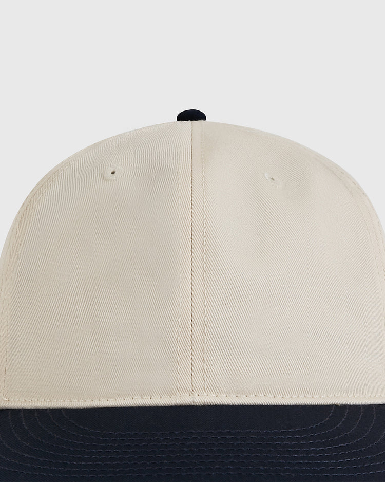 A front close-up of the Ebbets Field Natural and Navy Cotton Twill Ballcap, inspired by vintage baseball styles, with a beige crown, black brim, and photographed against a light gray background.