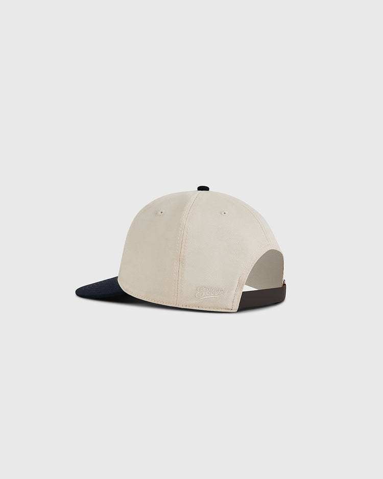 The Ebbets Field Natural and Navy Cotton Twill Ballcap is shown from the back and side on a light gray background. This vintage cap features a navy brim, adjustable strap, and visible stitching details.