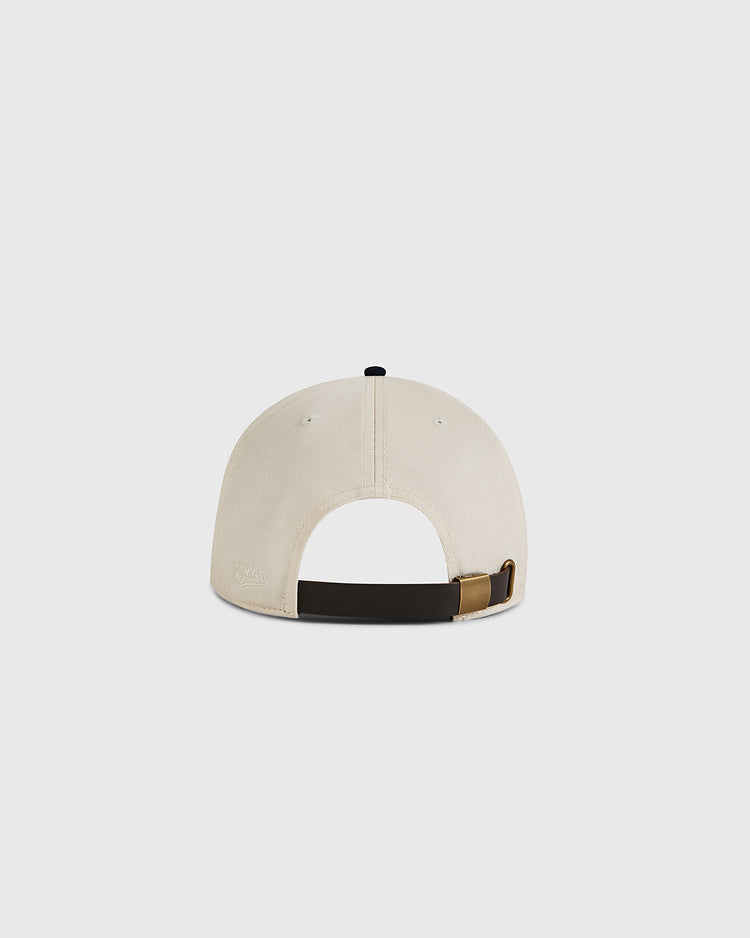 The Ebbets Field Natural and Navy Cotton Twill Ballcap is displayed from the back, highlighting its black adjustable strap with brass buckle and open section above, set against a plain white background.
