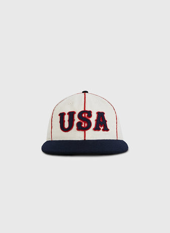 The Ebbets Field USA National Team 1936 Authentic Wool Ballcap features red stripes, bold red and blue USA lettering, and a dark blue brim, capturing the classic style of 1936 Olympic baseball on a white wool base.
