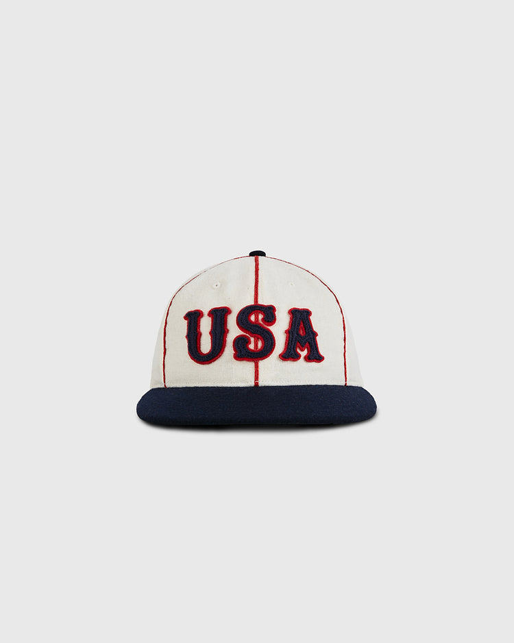The Ebbets Field USA National Team 1936 Authentic Wool Ballcap features red stripes, bold red and blue USA lettering, and a dark blue brim, capturing the classic style of 1936 Olympic baseball on a white wool base.