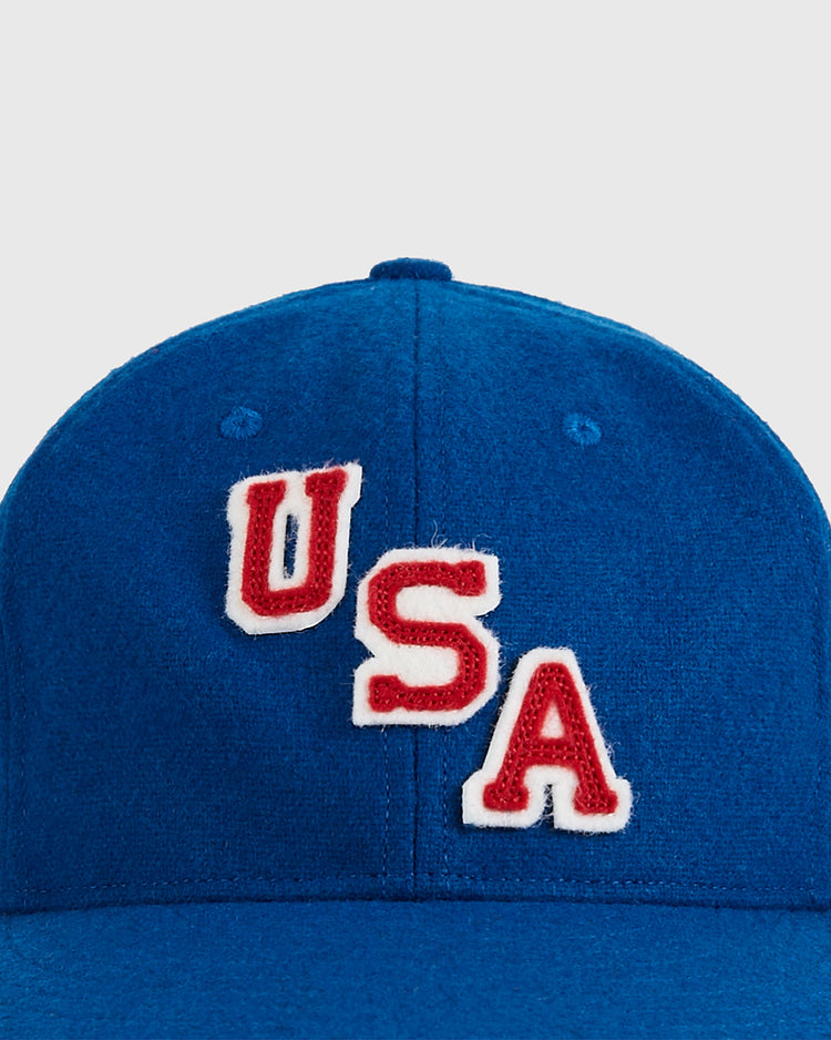 A close-up of the Ebbets Field USA Miracle On Ice 1960 Wool Ballcap, a vintage blue hat with red and white USA lettering sewn on the front, inspired by classic hockey history.