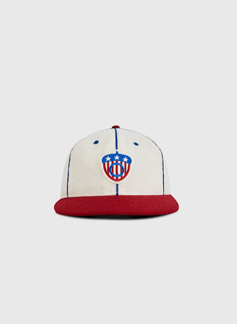 The Ebbets Field Oakland Oaks 1942 Authentic Wool Ballcap features a cream color, blue vertical stitching, red brim, and a front logo with a red, white, and blue shield inspired by the Pacific Coast League’s 1942 acorn and three white stars.