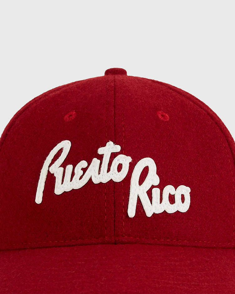 The Ebbets Field Puerto Rico 1958 National Team Wool Ballcap features “Puerto Rico” embroidered in white cursive on red wool, inspired by classic Puerto Rican baseball style.
