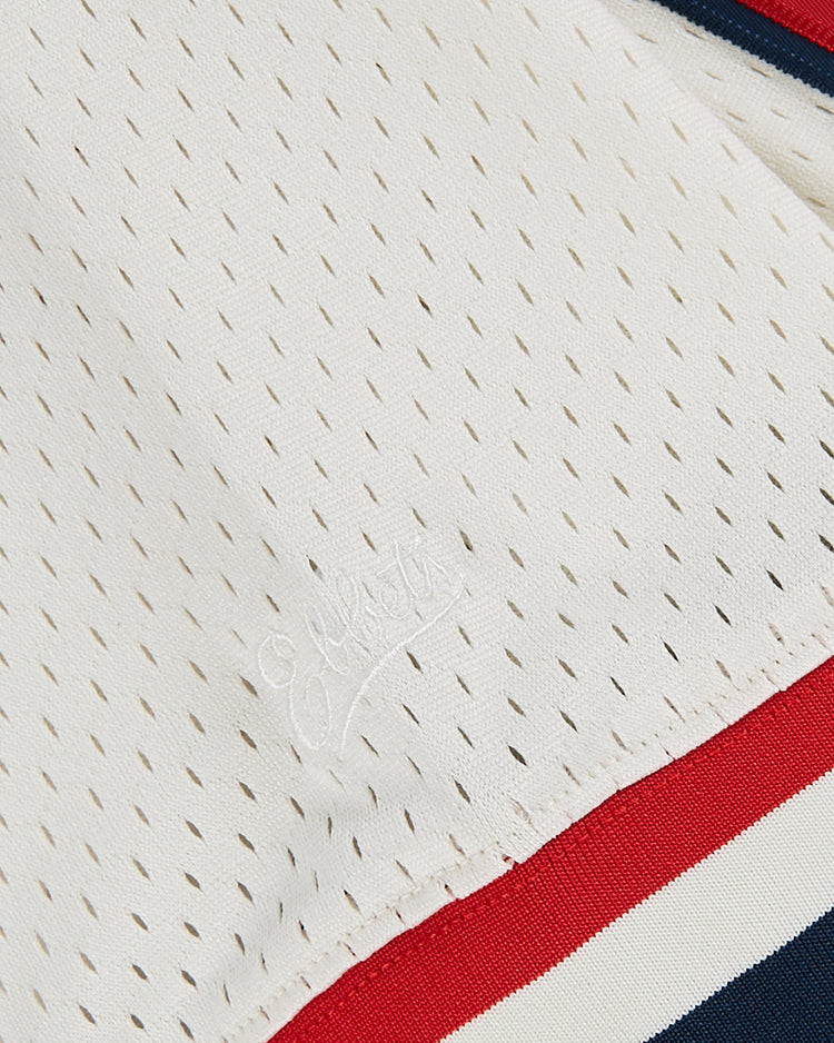 Close-up of the Ebbets Field USA National Team Mesh V-Neck Jersey's white perforated fabric, subtle embroidered lettering, and a red and navy striped trim along the edge.